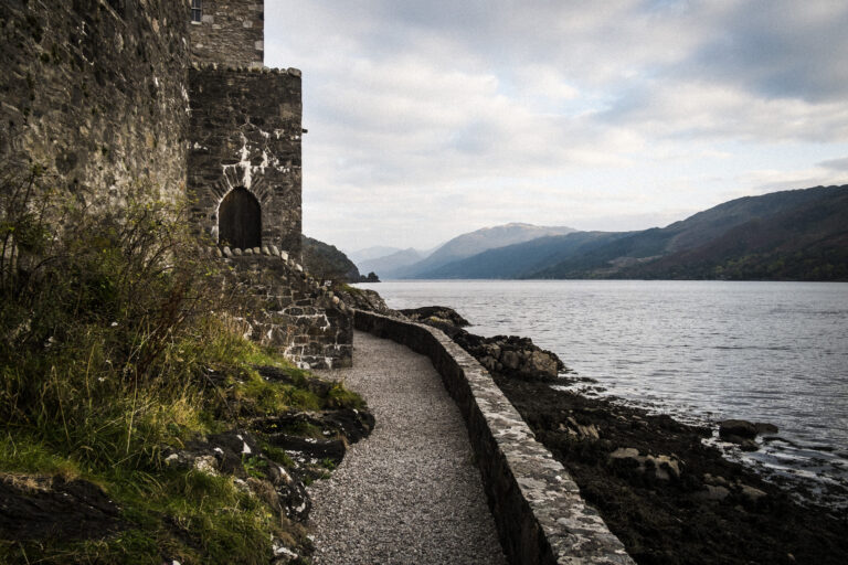 Castle in wall overlooking a loch with mountains in the distance.