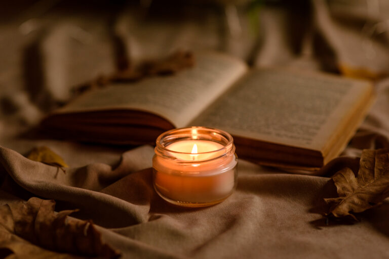 A burning candle on a wooden table in front of a book in a half-mast